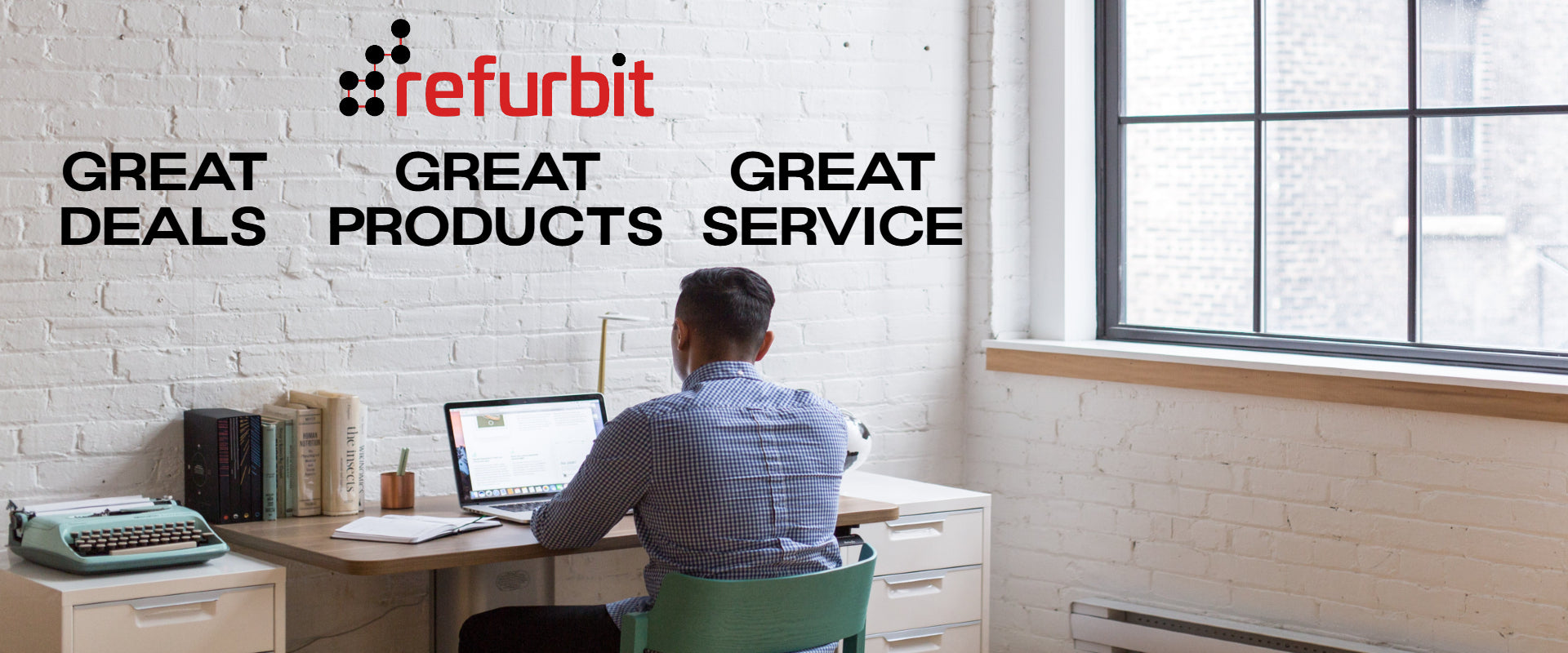 Person working at a desk with a window and white brick wall, featuring the Refurbit brand. Dell, HP, Lenovo, refurbished used computers.